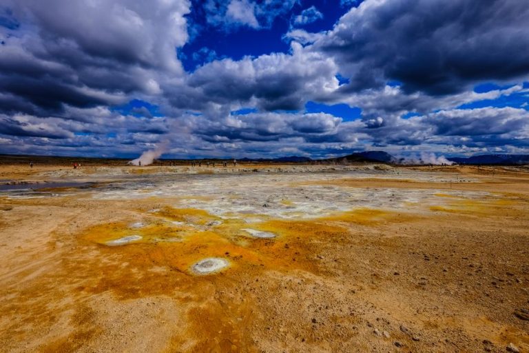 Vivid geothermal landscape with steam vents under a dramatic cloudy sky.