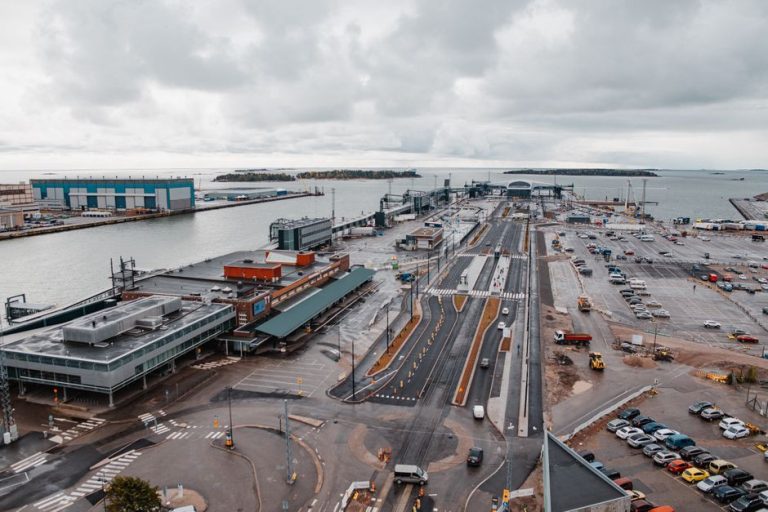 Aerial view of a busy industrial harbor with docks, warehouses, and vehicles near the sea.