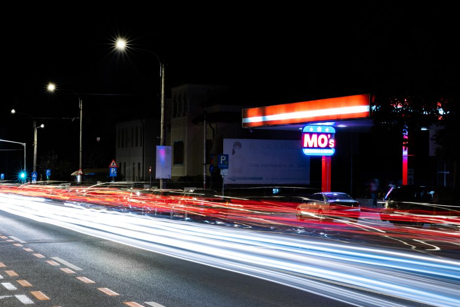 Long exposure of busy street at night in Sibiu, Romania, showcasing vibrant light trails and illuminated petrol station.