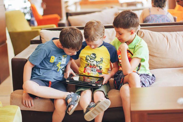Young boys sitting on a couch immersed in playing a game on a digital tablet indoors.