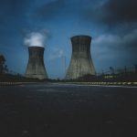 Moody view of industrial cooling towers with smoke against a twilight sky, emphasizing industry impact.