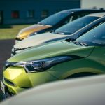 A row of brightly colored cars parked outdoors under daylight, showcasing their vibrant paint and shiny exteriors.