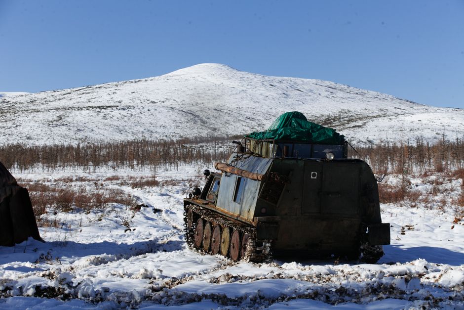 Cross country caterpillar vehicle parked on ground covered with snow near tent in mountainous area in winter