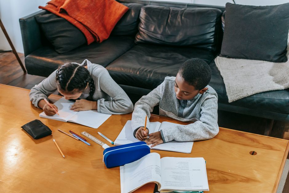 From above of concentrated diverse classmates sitting at table and doing homework assignment together