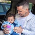A father lovingly feeds his baby with a milk bottle inside a car, showcasing warmth and care.