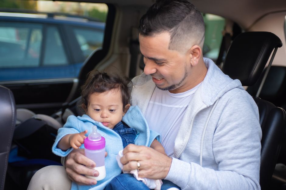 A father lovingly feeds his baby with a milk bottle inside a car, showcasing warmth and care.