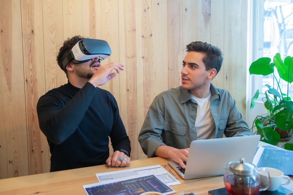 Two colleagues engage in a tech-savvy business meeting using virtual reality and laptops indoors.