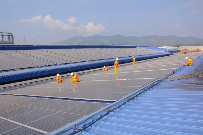 Workers installing solar panels on a large roof, highlighting renewable energy and sustainability.