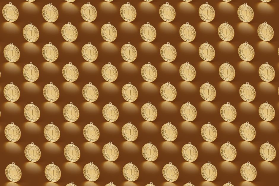 Multiple gold medals arranged in a repeating pattern on a brown backdrop.