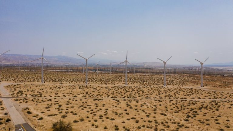 Aerial view of wind turbines in a vast desert landscape under a clear blue sky.