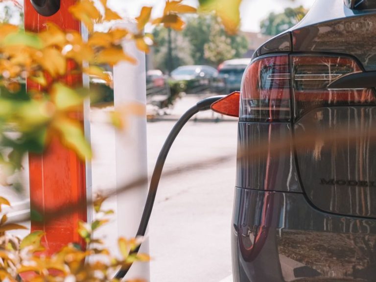 Close-up of an electric car charging at a station with blurred cars in the background.