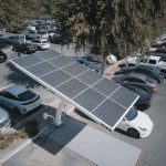 Electric cars charging at a solar-powered station in a parking lot.