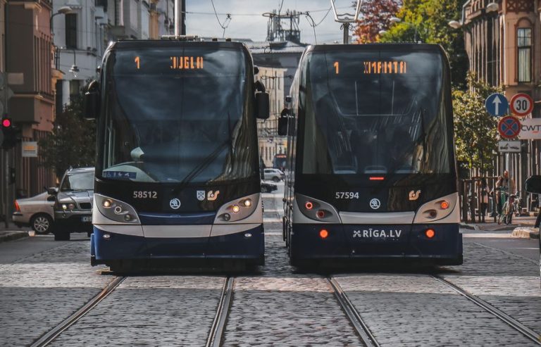 Two modern trams on cobblestone streets in Riga, Latvia, under a clear day sky.