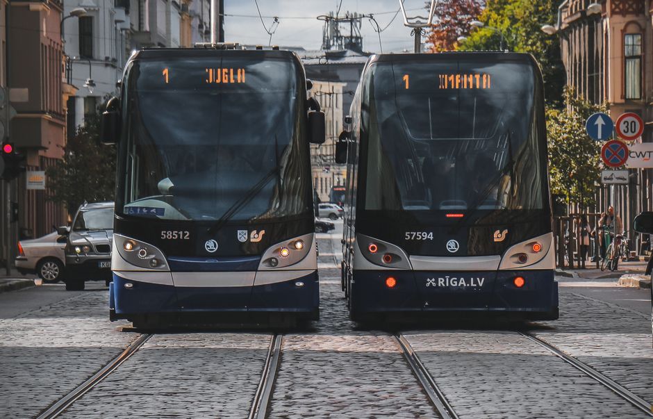 Two modern trams on cobblestone streets in Riga, Latvia, under a clear day sky.