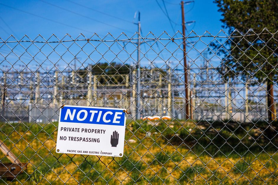 Chain link fence with a private property no trespassing notice sign and electrical infrastructure in the background.