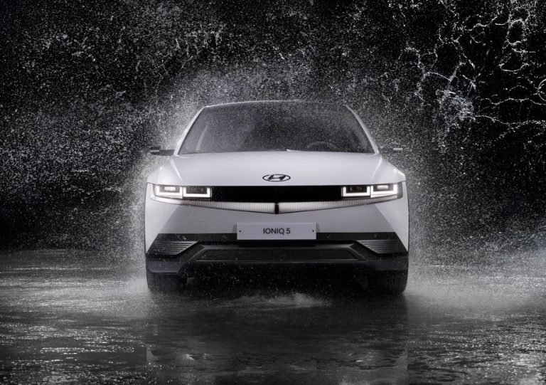 Dynamic front view of a Hyundai Ioniq 5 splashing through rain, captured in black and white.