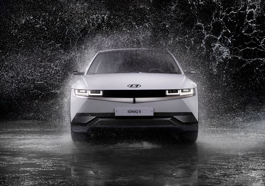 Dynamic front view of a Hyundai Ioniq 5 splashing through rain, captured in black and white.