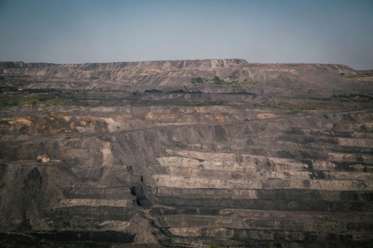 A vast open-pit coal mine under a clear blue sky, showcasing industrial landscape and natural rock formations.