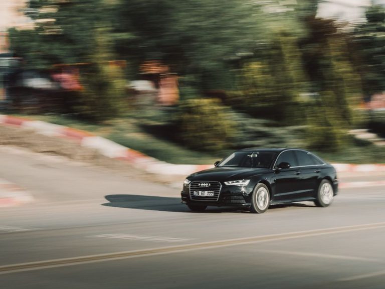 Dynamic shot of a black Audi car on a city road, emphasizing speed and motion.