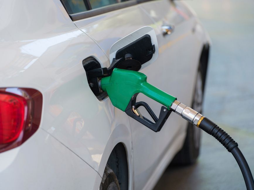 Close-up of a green nozzle refueling a white car at a gas station.