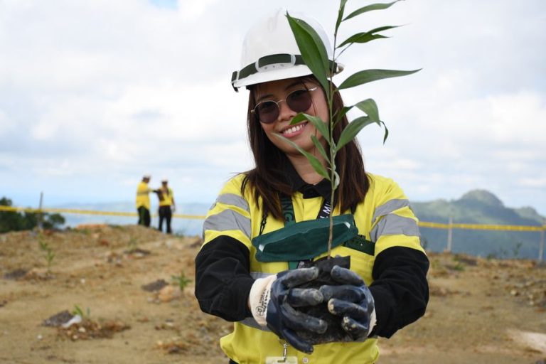 Smiling woman holding a young plant at a construction site in Toledo City, Philippines.