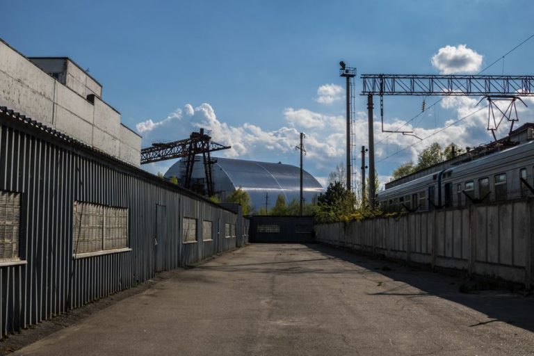 View of Chernobyl's new safe confinement and railway tracks under a blue sky.