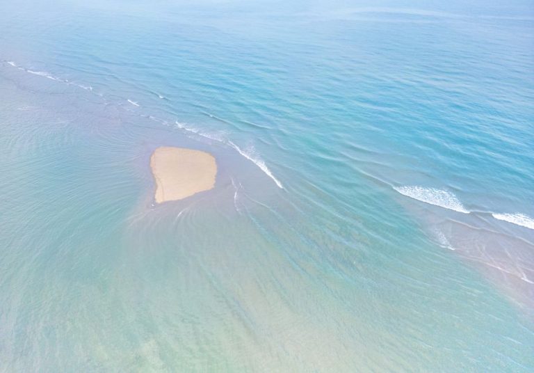 Drone captures a sandy shoal surrounded by clear turquoise waters, highlighting serenity.