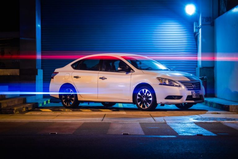 A white car parked in an urban setting at night, illuminated by vibrant red and blue light trails.