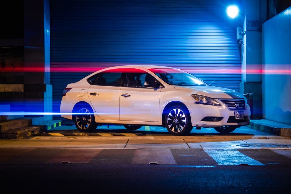 A white car parked in an urban setting at night, illuminated by vibrant red and blue light trails.