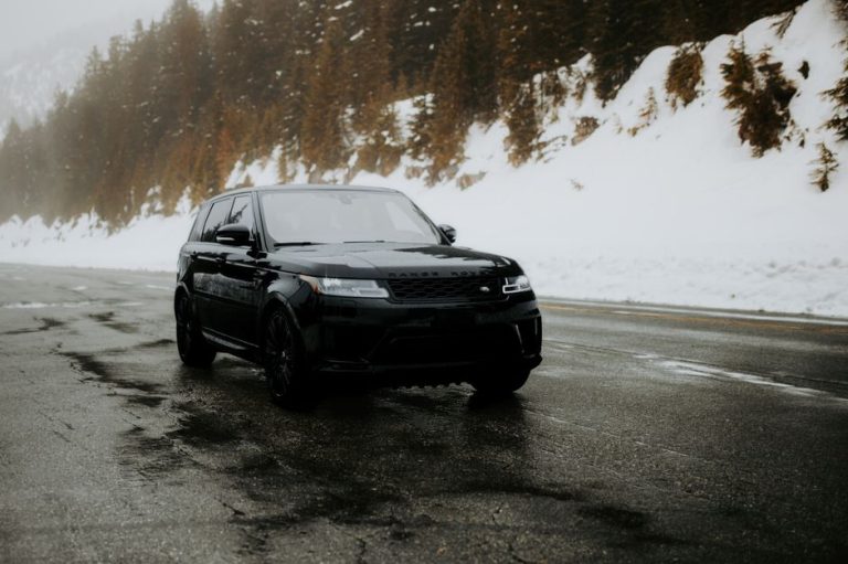 A sleek black SUV navigates a wet, snow-covered mountain road surrounded by evergreen trees.