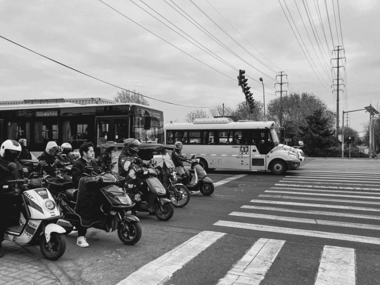 Black and white image of a city intersection with scooters and buses at a crosswalk.