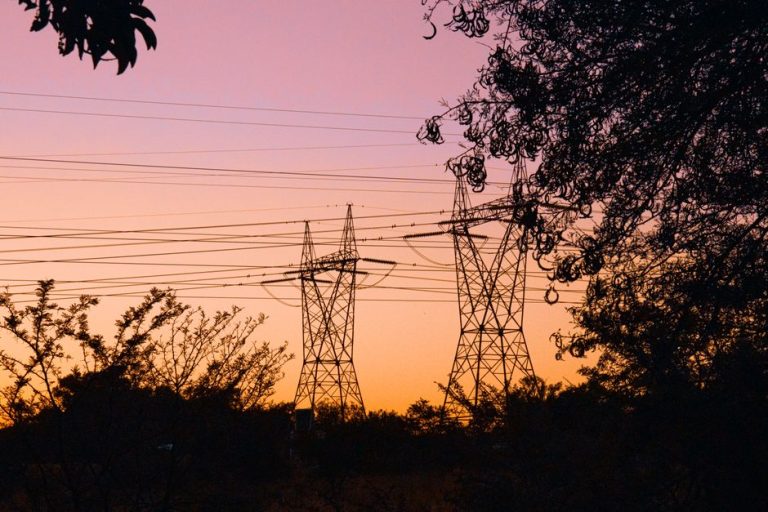 Silhouetted transmission towers at sunset surrounded by trees, creating an evocative scene.