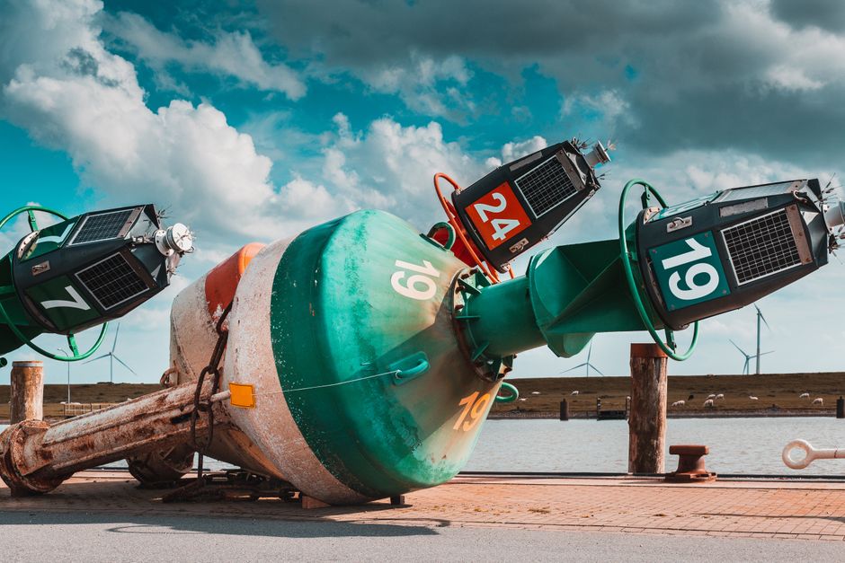 Vibrant photo of dockside buoys with wind turbines and cloudy sky in background.