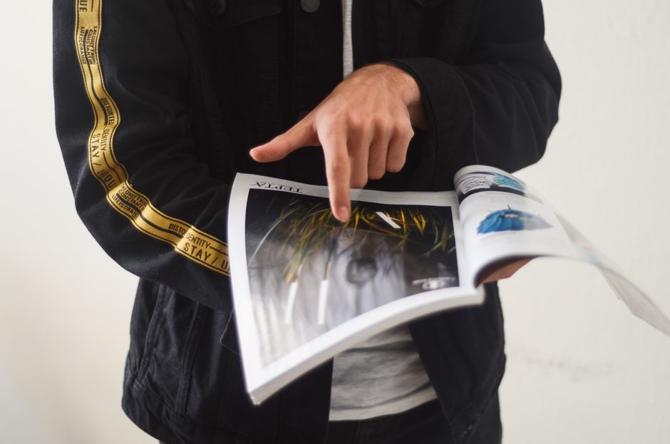 Close-up of a person pointing at a page in an open magazine. Ideal for editorial content.
