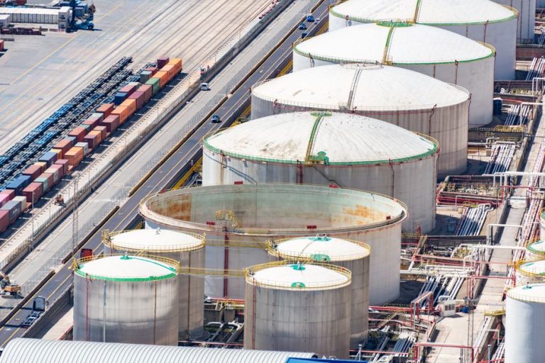 Aerial shot of large oil storage tanks in an industrial district with adjacent railway tracks.