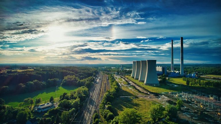 Aerial view of the Dětmarovice power plant amidst greenery under a bright blue sky.