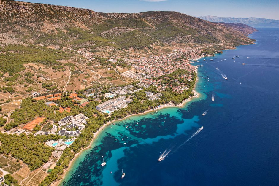 A stunning aerial view of a town by the Adriatic Sea with turquoise waters and lush green hills.