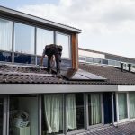 Technician working on installing solar panels on a residential rooftop during the day.