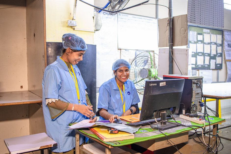 Two female textile workers smiling at their desk in a factory setting.