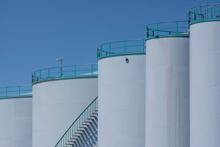 Large industrial storage tanks with green railings against a clear blue sky.