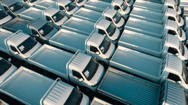 Aerial view of white pickup trucks parked in rows, emphasizing symmetry and industrial style.