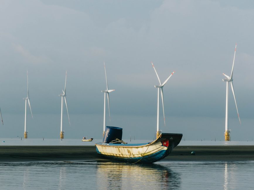 A peaceful coastal scene with a fishing boat and wind turbines on a calm sea.