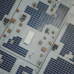 High-angle aerial shot of a large rooftop solar panel array on an industrial building.