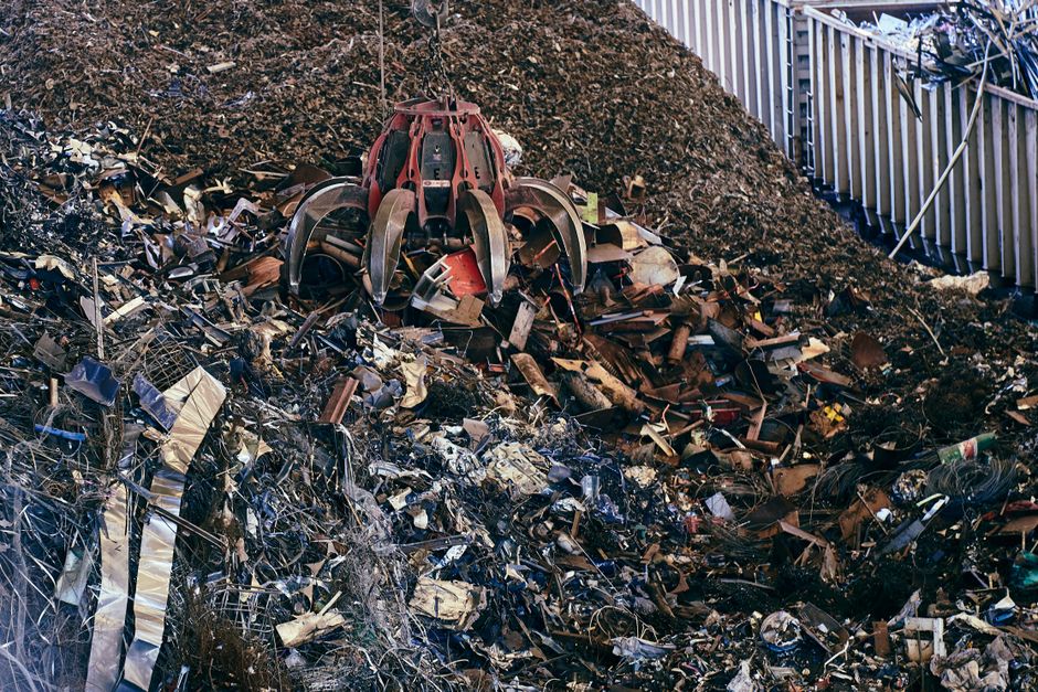 A claw excavator sifting through a large pile of industrial scrap metal outdoors.