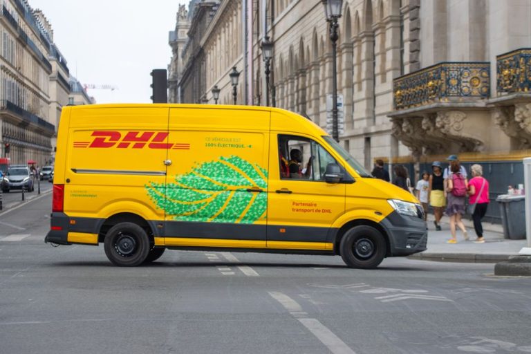 Electric delivery van navigating through a busy Parisian street on a sunny day.