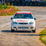 A rally car speeds through a curvy track surrounded by greenery in Ritsona, Greece.