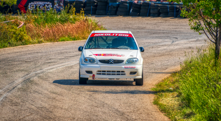 A rally car speeds through a curvy track surrounded by greenery in Ritsona, Greece.