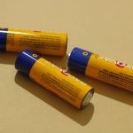 Three AA alkaline batteries on a beige surface, representing power and energy storage.