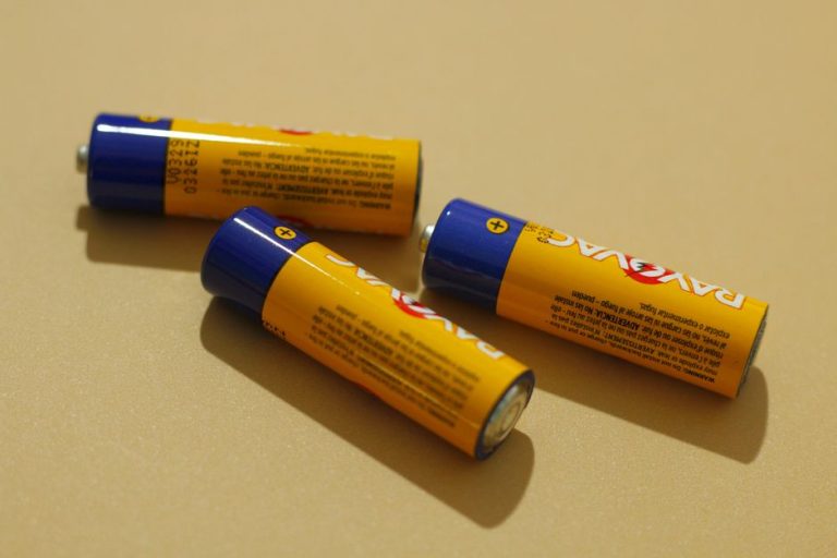 Three AA alkaline batteries on a beige surface, representing power and energy storage.