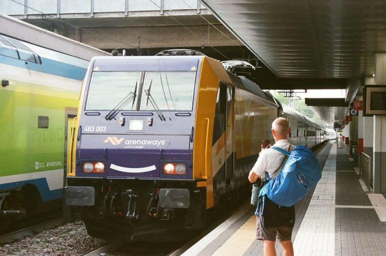 A traveler with a backpack waits beside a traxx train at a station in Milan.